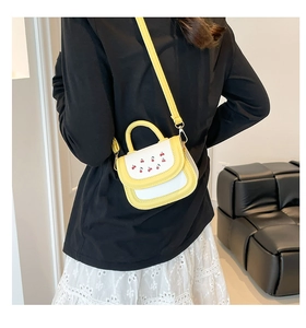 Détail du sac bandoulière jaune et blanc avec broderie cerise porté par un mannequin