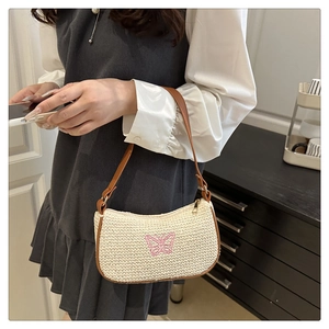 Détail de la broderie papillon rose sur le sac sous l'aisselle en paille crème avec zip doré