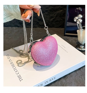 Detail of pink glitter heart-shaped bag with silver chain strap on a white book