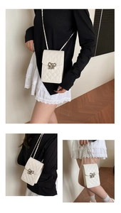 Close-up of beige quilted crossbody phone bag with silver bow accent and chain strap