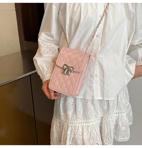 Detail shot of a pink quilted phone bag with a silver bow accent and chain strap
