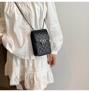 Detailed view of black quilted leather crossbody phone bag with silver bow charm and chain