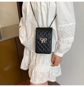 Detail of black quilted mini crossbody bag with silver bow and chain strap on model