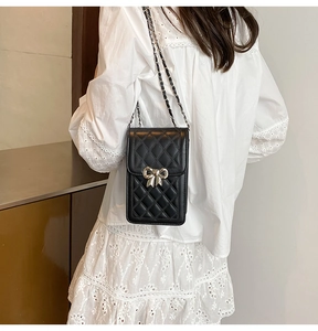 Detail of black quilted leather phone bag with silver bow accent and chain strap