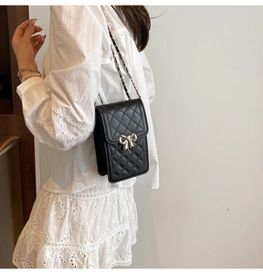 Close-up of quilted black leather phone bag with silver bow and metal chain strap