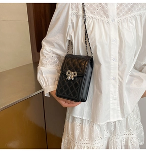 Close-up of black quilted leather mini bag featuring a silver bow buckle and chain strap