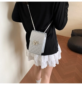 Silver quilted crossbody phone bag with chain strap shown on model in minimalist interior
