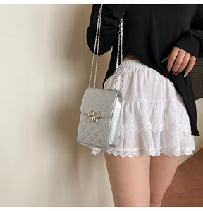 Silver quilted crossbody bag with metal bow detail shown on shoulder with chain strap