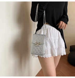 Detail of silver quilted phone bag with metal bow buckle and elegant chain strap