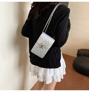 Detailed view of silver quilted cell phone bag with bow clasp and chain strap on a model