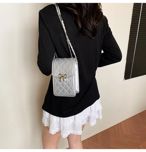 Silver quilted mini crossbody bag with metal bow detail and chain strap shown on model