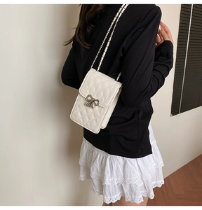 Detailed view of white quilted mini crossbody bag with silver bow buckle on model