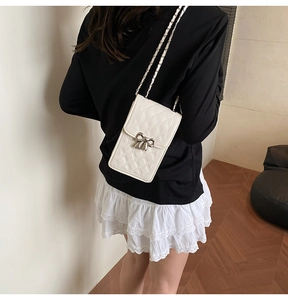 Mini white quilted phone bag with silver bow and chain strap on a model's shoulder