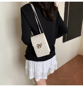 Close-up of white quilted mini crossbody bag with silver bow accent and chain strap