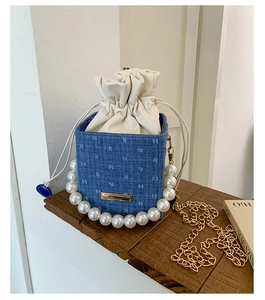 Detailed view of denim bucket bag with pearl handle and golden chain on wooden surface