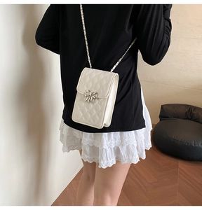 White quilted mini crossbody bag with silver bow detail and chain strap on a model