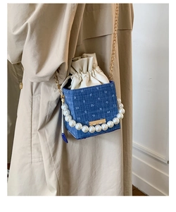 Close-up of blue denim crossbody bag with pearl handle and chain strap on beige coat