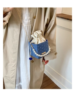 Close-up of blue denim bucket bag with pearl handle and golden chain strap detail
