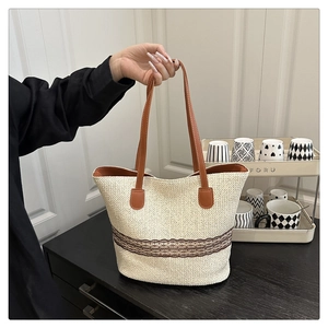 Detail of woven straw tote bag featuring brown lace band and faux leather handles