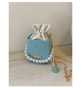 Detail of mint green textured bucket bag featuring pearl handle and gold chain strap
