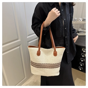 Detail shot of a large woven tote bag with brown leather handles and contrast trim detailing