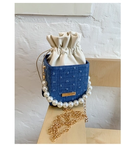 Detail of blue denim bucket bag with large pearl handle and golden chain strap