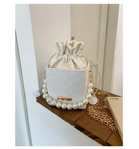 Detail of drawstring bucket bag with pearl handle and golden chain on wooden stand