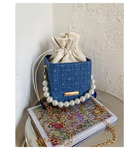 Detailed close-up of blue denim woven bucket bag with pearl handle and gold chain strap