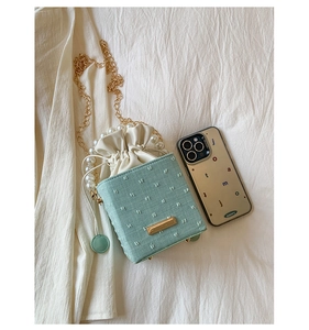 Detail of mint green textured crossbody bag with pearl handle and golden chain strap