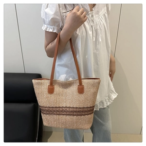 Detail of a large woven straw tote bag with brown lace stripes and leather handles