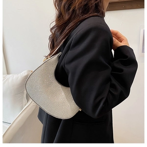 Sac hobo argenté brillant avec strass porté à l'épaule sur un tailleur noir chic