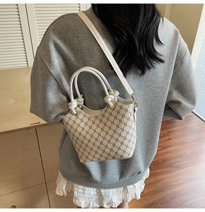 Détail d'un sac seau crème à motif de chaîne et bandoulière porté par un mannequin
