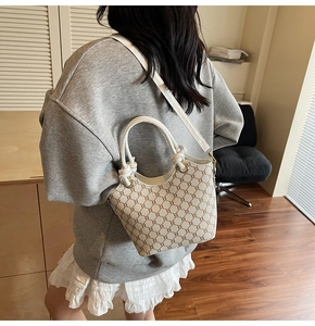 Détail du sac seau monogramme blanc et marron porté par un mannequin dans un décor intérieur