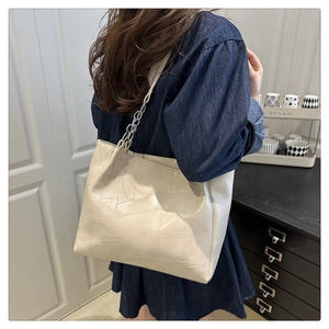 Detail of off-white faux leather tote bag with geometric texture and silver chain strap