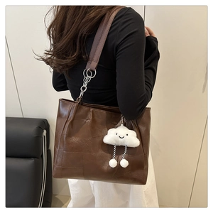 Close-up of large dark brown leather tote bag with white cloud plush charm and patchwork texture