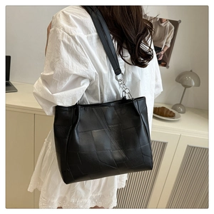 Detail of black patchwork tote bag with stylish metal chain and leather shoulder strap
