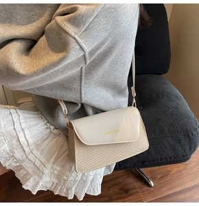 Detail of cream crossbody bag showing leather flap with gold text and woven texture