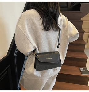 Detailed view of a black flap crossbody bag with textured stripes on gray sweatshirt