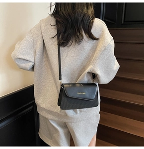 Detail of a black crossbody bag with gold lettering shown on a model in a grey hoodie