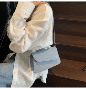 Close-up of light blue flap crossbody bag featuring woven leather textures and gold lettering