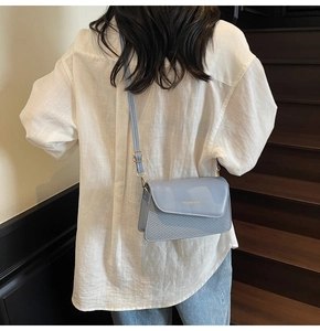 Detail of light blue textured leather crossbody bag with gold metal logo and strap buckle