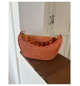 Detail of orange woven dumpling bag with amber resin bead strap on wooden surface