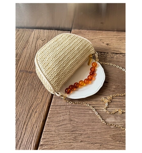 Detail of mini woven bag with amber bead handle and gold metal chain on wood