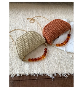 Close-up of woven straw dumpling bags with amber bead handles and metal chain straps