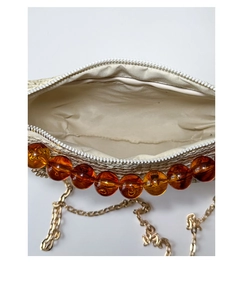 Close-up of woven straw shoulder bag with orange beads, white zipper and gold chain strap