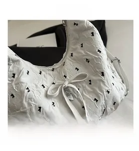 Close-up of white quilted tote with black bow embroidery and silver heart charm