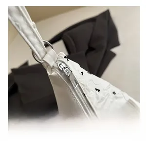Close-up of smooth silver zipper and bow embroidery on white leather handbag detail