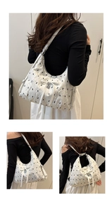 Detail of white pleated tote bag featuring a silver heart pendant and ribbon bow