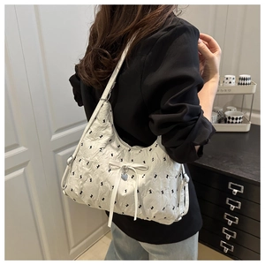 Close-up of white pleated shoulder bag with black bows and a silver heart pendant