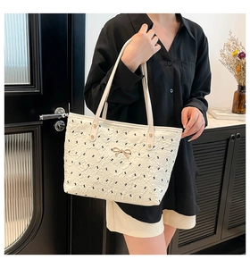 Detail of a beige tote bag featuring bow embroidery and a golden metal bow clasp detail